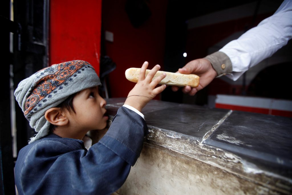 عامل يعطي خبز لطفل يمني في صنعاء
