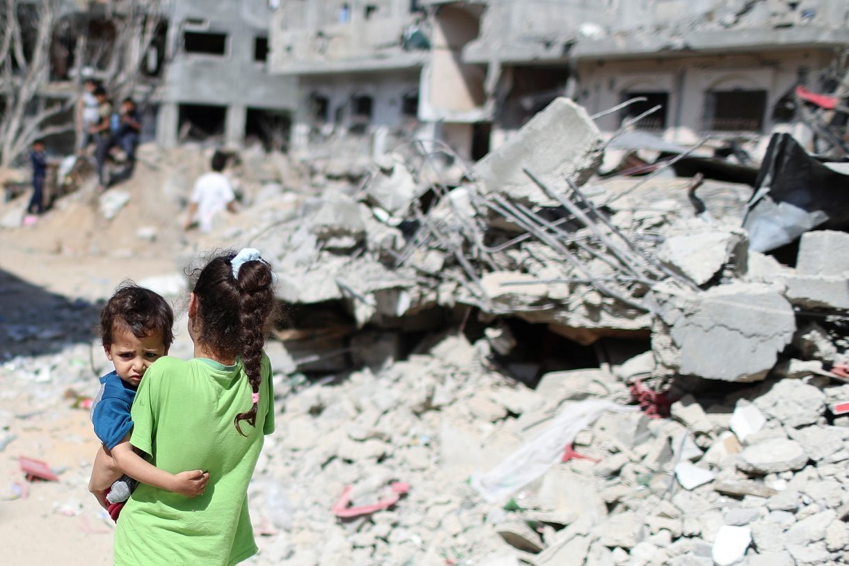 فتاة فلسطينية تحمل طفلاً أمام أنقاض منازلهم التي دمرتها الغارات الجوية الإسرائيلية على غزة/رويترز