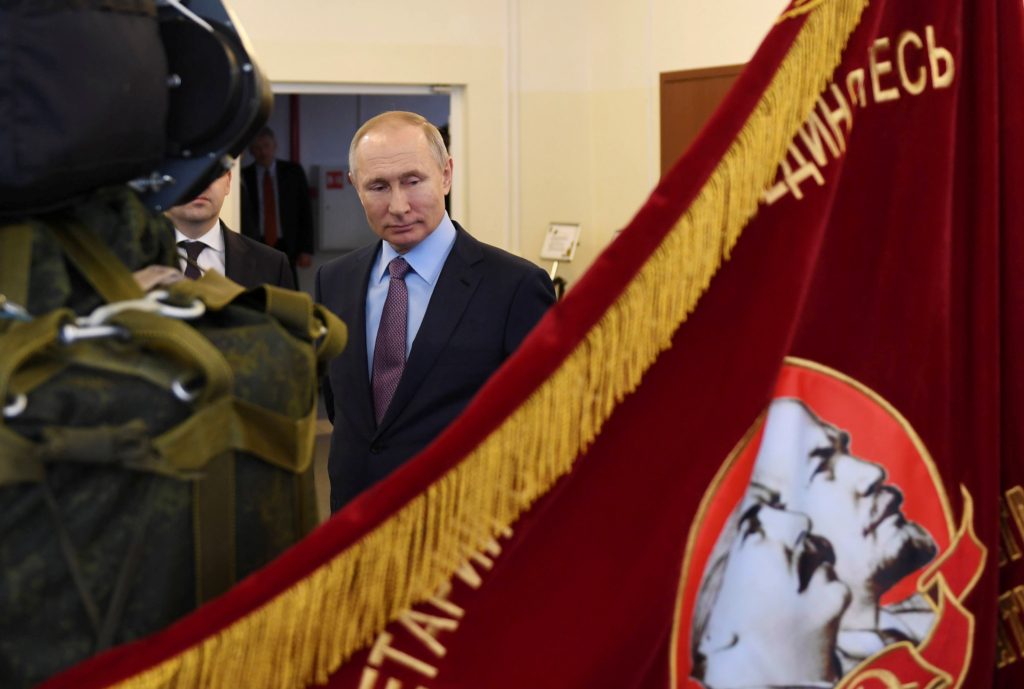 الرئيس الروسي فلاديمير بوتين، وراية تحمل صور قادة الاتحاد السوفييتي التاريخيين/ رويترز