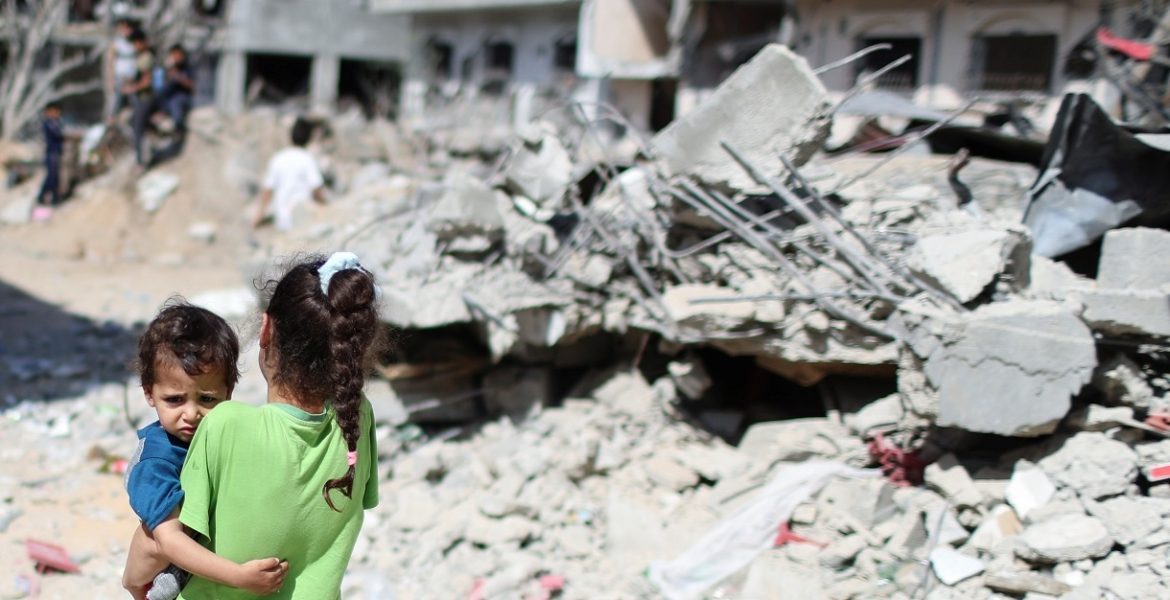فتاة فلسطينية تحمل طفلاً أمام أنقاض منازلهم التي دمرتها الغارات الجوية الإسرائيلية على غزة/رويترز